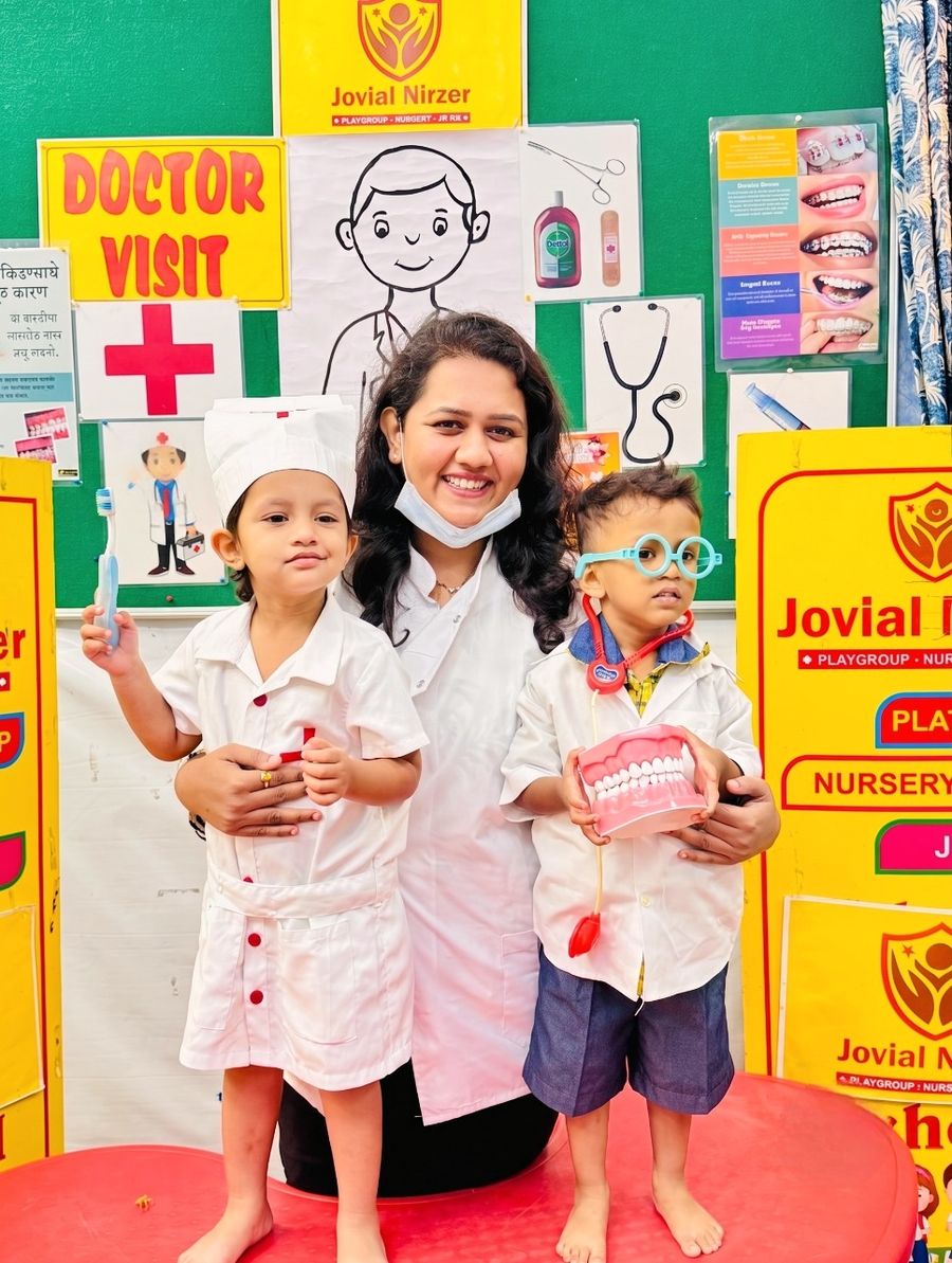 Dr. Shraddha with two young children dressed as little doctors at a school dental activity