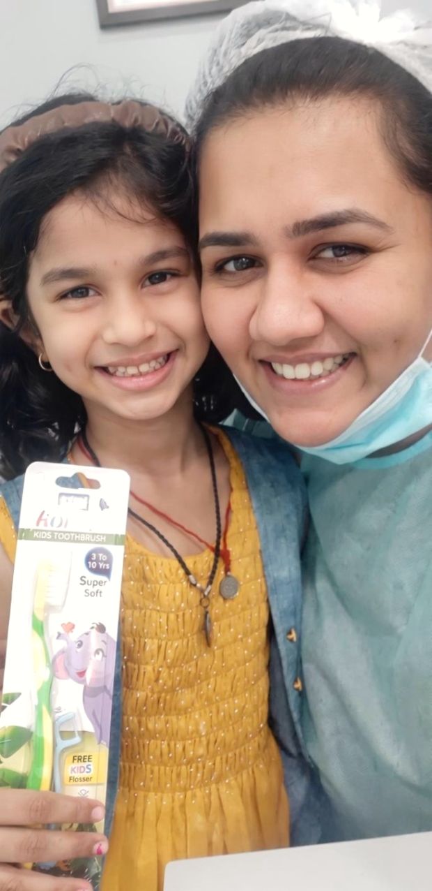 A young patient smiling with her new children's toothbrush beside Dr. Shraddha