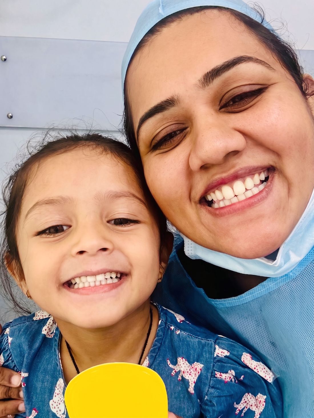 Dr. Shraddha cheek to cheek with a smiling little girl holding a yellow cup