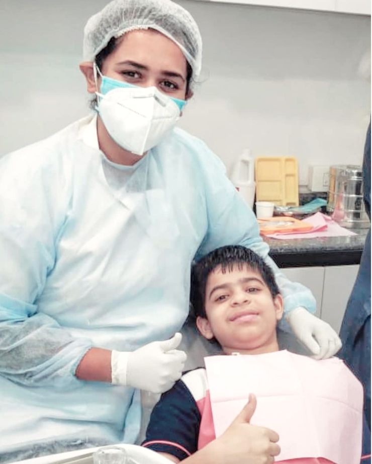 A young patient in the dental chair giving a cheerful thumbs-up beside Dr. Shraddha