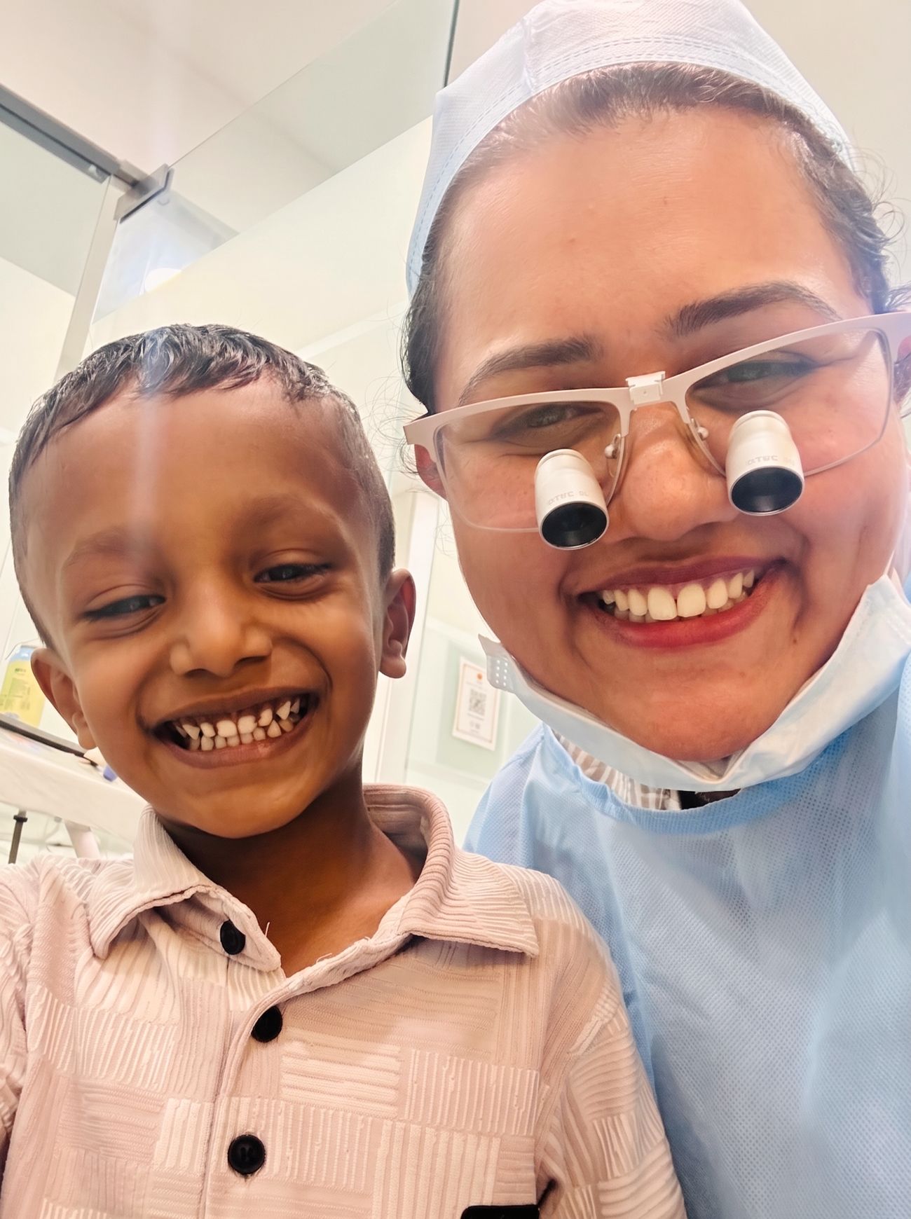 Dr. Shraddha, wearing dental loupes, sharing a selfie with a smiling young patient at Crown Dental Care