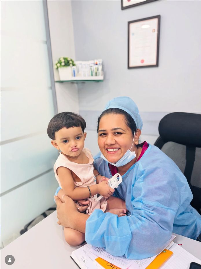 Dr. Shraddha holding a toddler patient at the clinic desk, both at ease